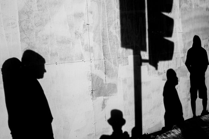 Shadows of people cast on a textured wall in a candid street photo capturing the quiet beauty of everyday life.