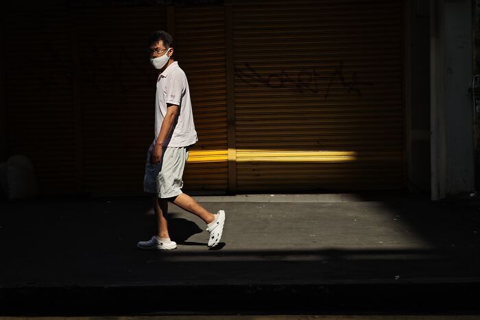 Man wearing mask walking past shuttered storefront in candid street photo capturing quiet beauty of everyday life