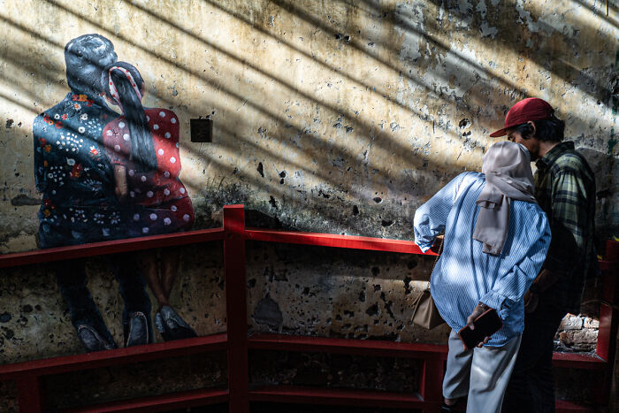 Couple in casual clothes photographing wall art, showcasing candid street photos capturing quiet beauty of everyday life.