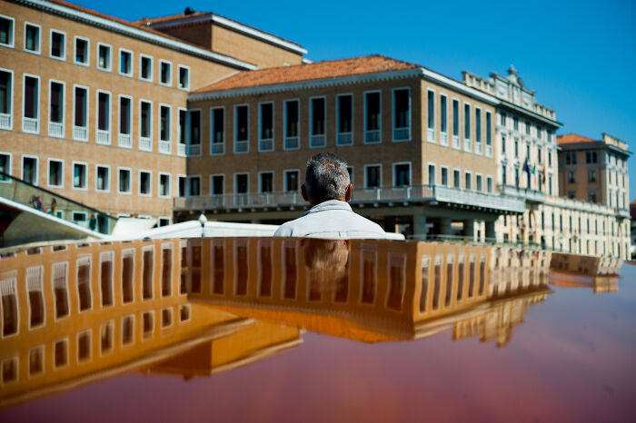 Man sitting with his back facing the camera, reflected on a shiny surface, with cinematic photos capturing everyday life.