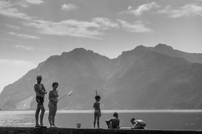 Black and white cinematic photo of a family by the lake with mountains in the background capturing everyday life moments.