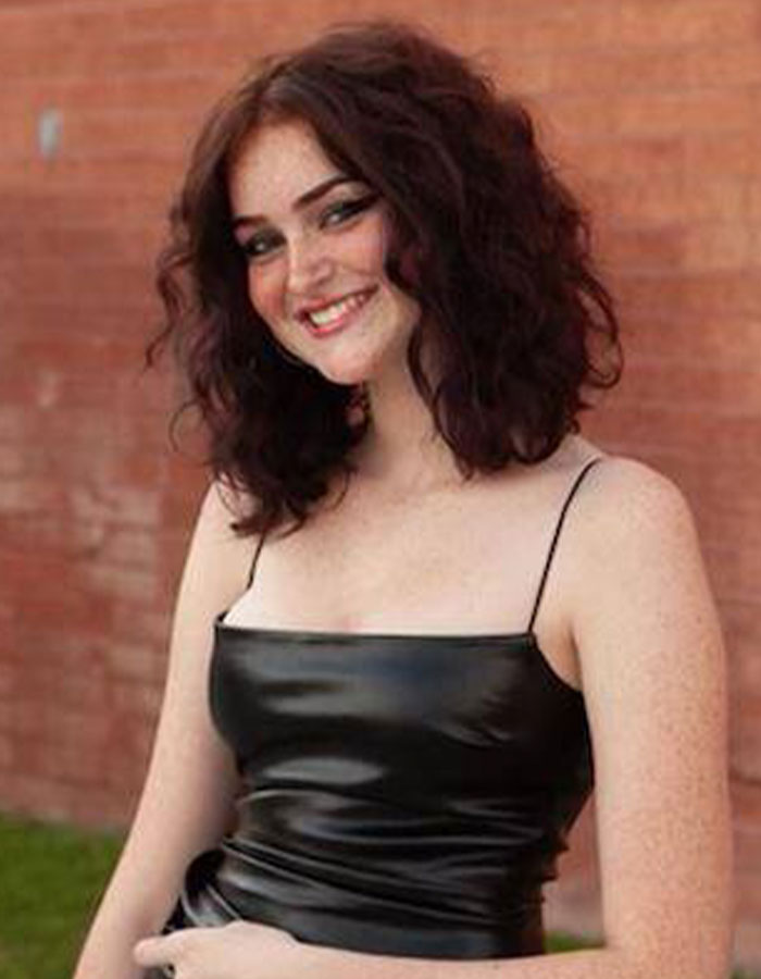 Young woman smiling outdoors against a brick wall, related to parents warning about dusting challenge dangers.