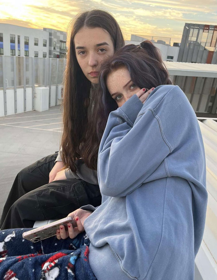 Two young women sitting outdoors at sunset, expressing concern and sharing a warning about the dusting challenge dangers.