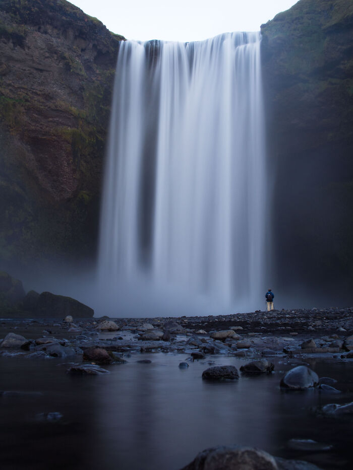 Majestic waterfall with a person standing nearby, showcasing breathtaking travel photos capturing nature's beauty.