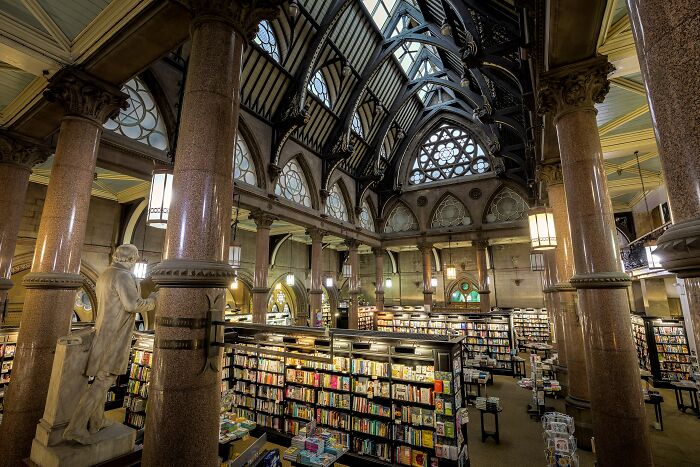 Grand interior of a stunning bookstore with tall columns, arched windows, and rows of shelves filled with books.