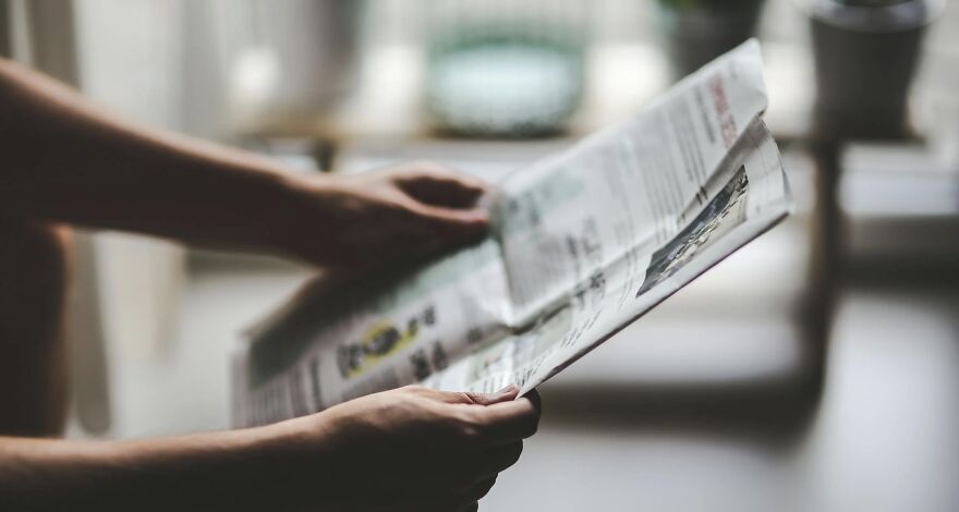 Person holding and reading a newspaper indoors, illustrating a then vs. now poll comparison concept.