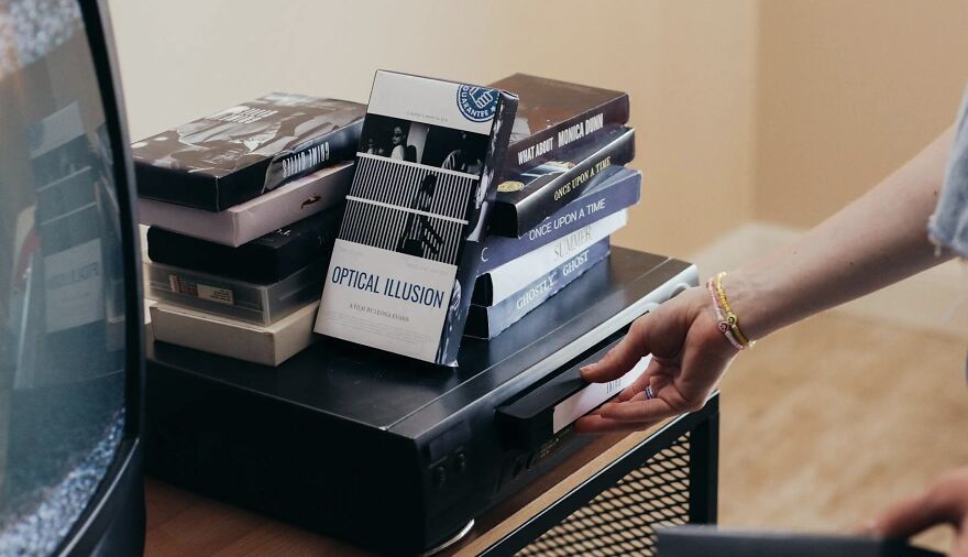 Hand inserting a VHS tape into a player with a stack of tapes nearby, illustrating a Then vs. Now poll concept.