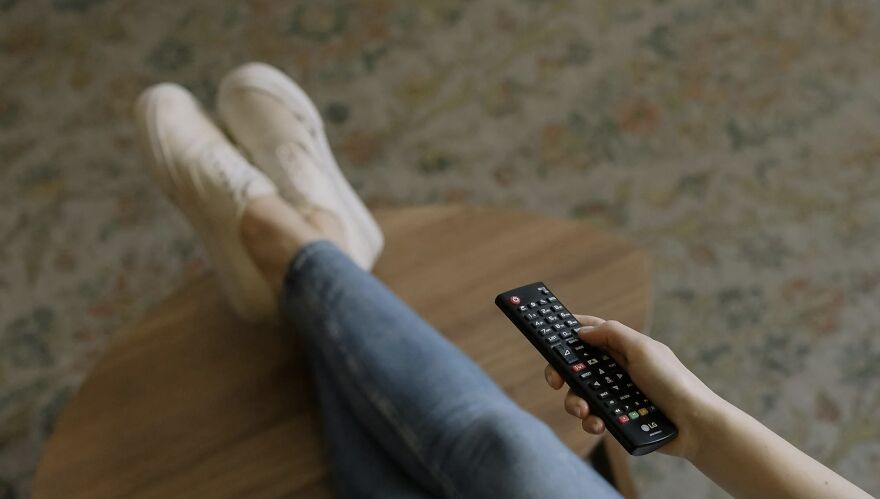 Person holding a remote control with legs crossed on a table representing a then vs now poll comparison.
