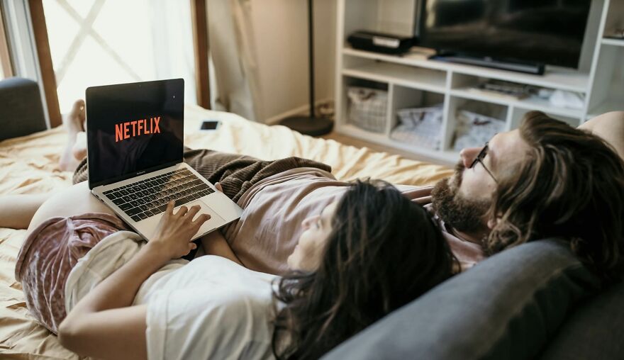 Couple relaxing on a couch watching Netflix on a laptop, illustrating entertainment habits for Then vs Now poll.