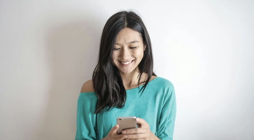 Young woman smiling while holding a smartphone, participating in a then vs now poll in a bright setting