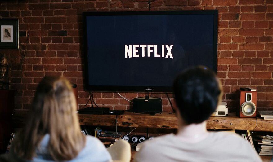 Two people watching Netflix on a TV in a cozy room with exposed brick walls in a then vs now poll context.