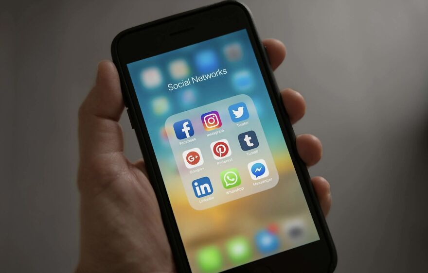 Hand holding smartphone displaying social networks folder with popular apps for then vs. now poll discussion.