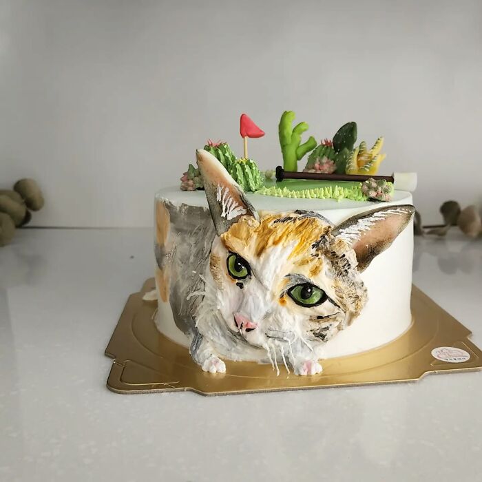 3D pet-themed cake featuring a detailed cat face with green eyes and decorative cactus designs on top.