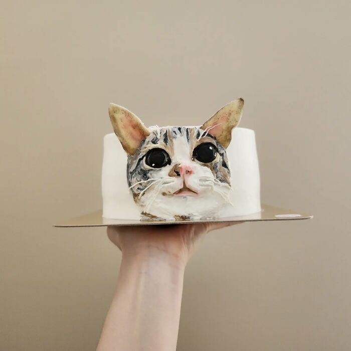 Hand holding a pet-themed cake resembling a cat with large eyes, showcasing adorable cake art capturing pet personality.
