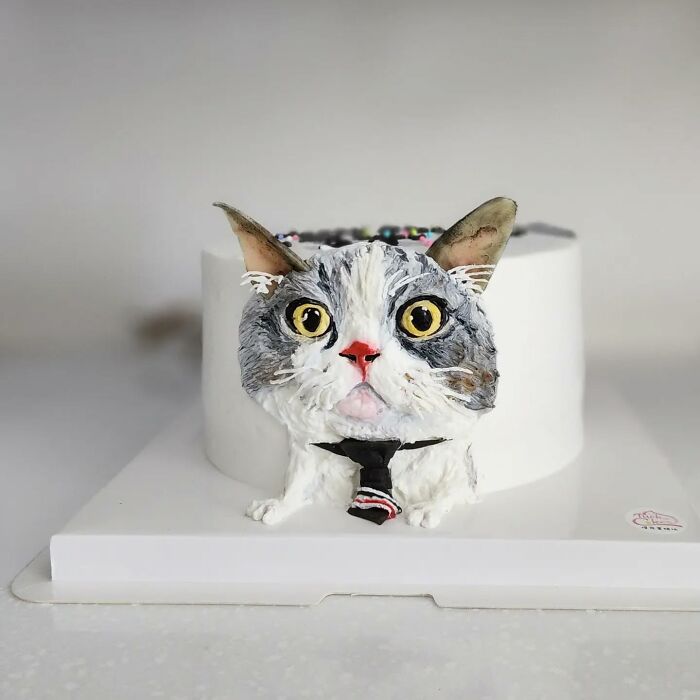 Pet-themed cake featuring a detailed cat face with big yellow eyes and a small black tie, capturing unique personality.