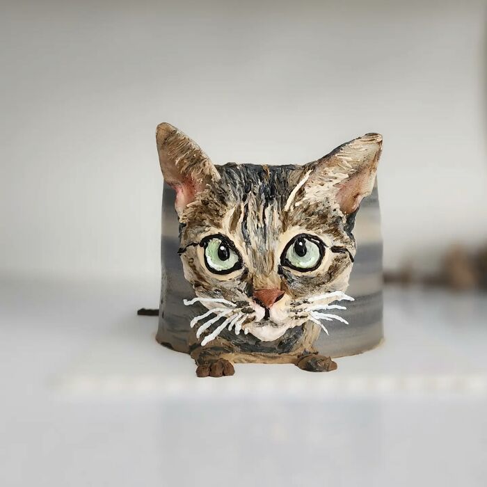 Realistic pet-themed cake shaped like a cat head with detailed fur and large green eyes, showcasing unique personality.