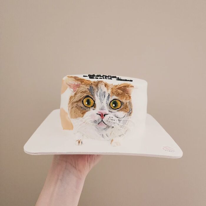 Hand holding a pet-themed cake featuring an adorable, realistic cat face capturing its unique personality.