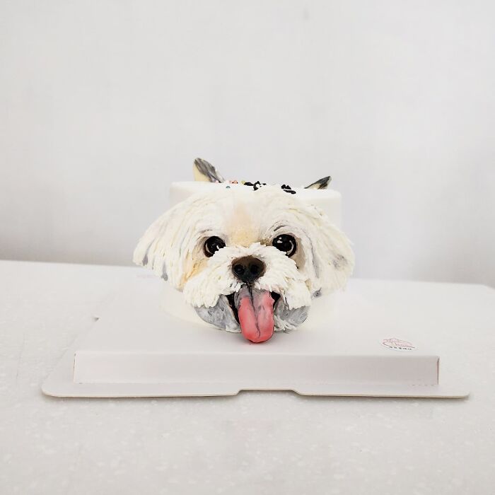 Realistic pet-themed cake shaped like a white dog with a pink tongue, showcasing artist-made adorable pet cake design.
