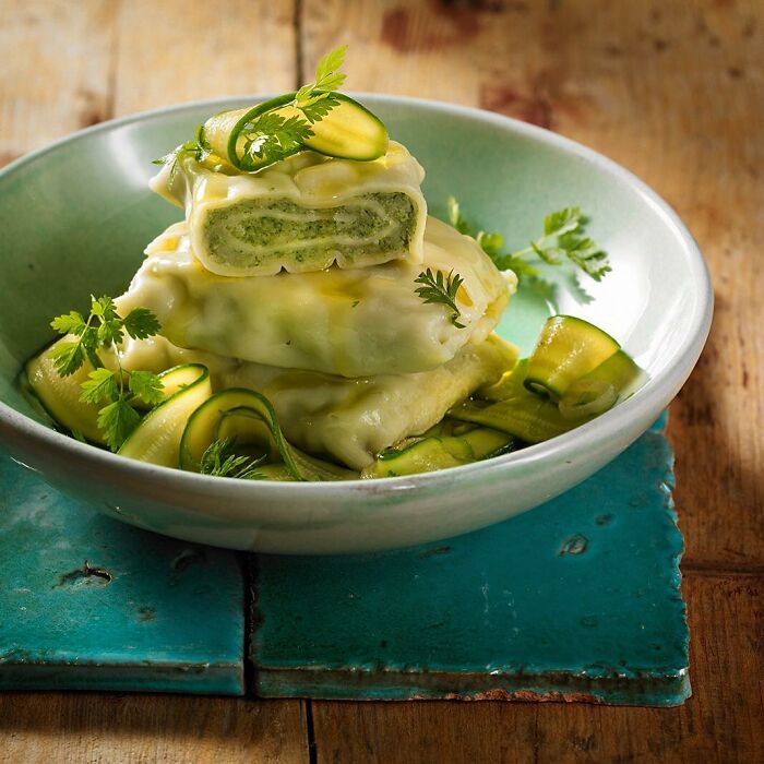 Creamy green-filled pasta with fresh herbs and thin cucumber slices served in a green bowl, mouthwatering food photo by Kai Stiepel.