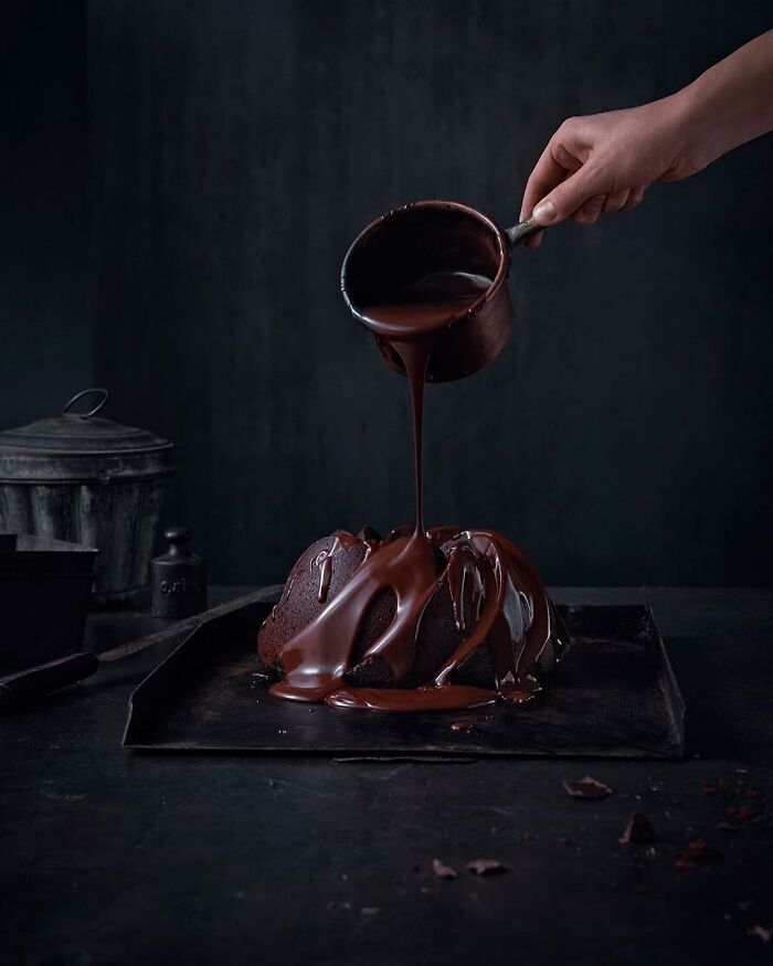 Hand pouring rich chocolate sauce over moist chocolate cake, a mouthwatering food photo by Kai Stiepel that might make you hungry instantly.
