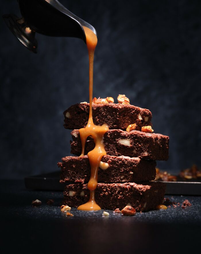 Stack of chocolate brownies with nuts topped by caramel sauce being poured, mouthwatering food photo by Kai Stiepel.