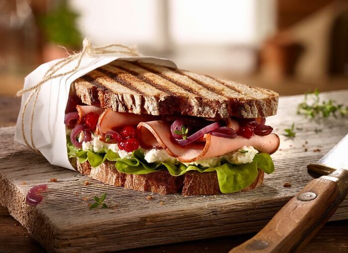 Grilled sandwich with ham, lettuce, onions, and cheese on rustic bread displayed in a mouthwatering food photo by Kai Stiepel.