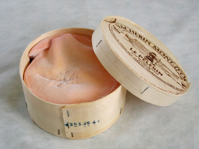 Wheaty rind cheese in wooden box, one of the surprising foods that are banned in the USA displayed on a light surface.