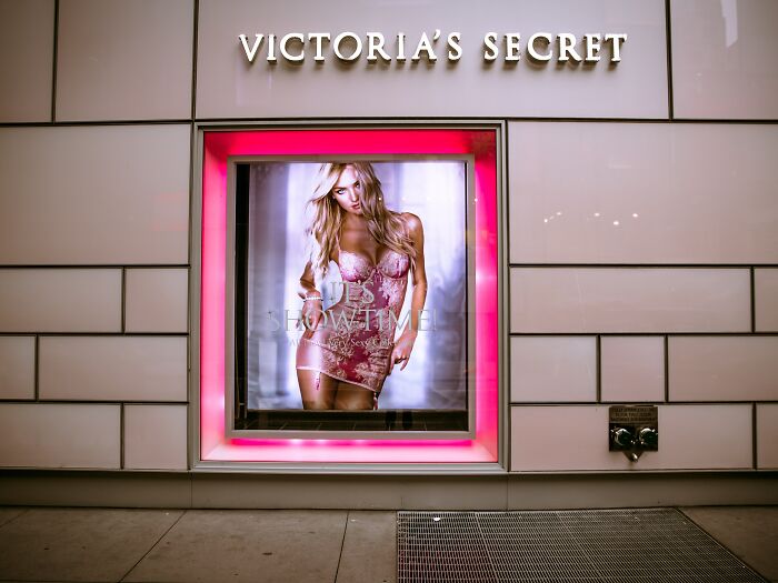 Victoria's Secret storefront with a glowing pink frame featuring a model in lingerie, highlighting sneaky terms and conditions.