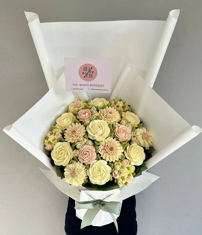 Bouquet of baked goods resembling a flower bouquet with pastel-colored frosting flowers wrapped in white paper.