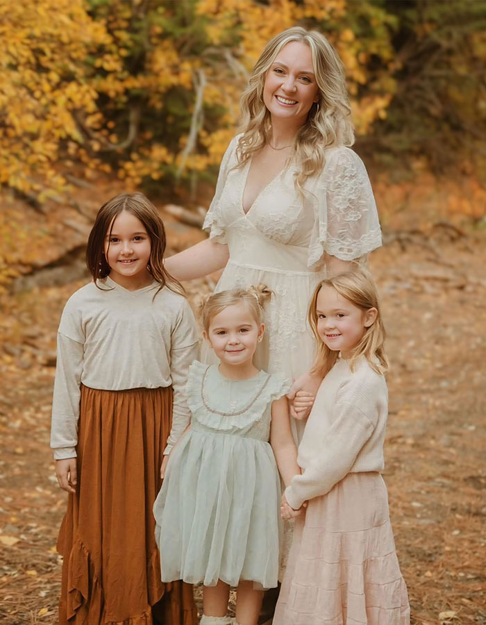 Mother and three daughters smiling outdoors in autumn woods after horrifying suffocation incident involving dad.