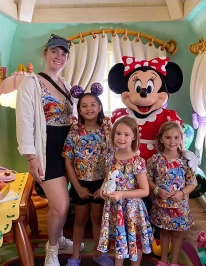 Woman and three girls wearing cartoon character outfits posing with Minnie Mouse in a colorful themed room after tragic family event.