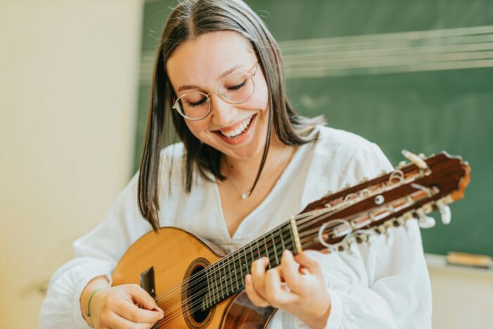 Young woman happily playing guitar, one of the everyday items under $300 that improved people’s lives.