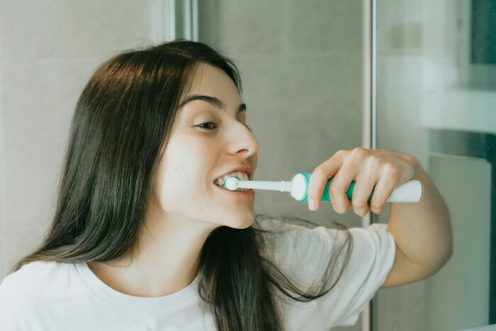 Woman using an electric toothbrush in bathroom, demonstrating one of the everyday items under $300 that improve lives.