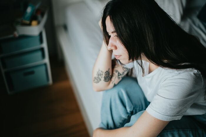 A pensive woman with tattoos sitting on the floor by a couch, reflecting on unresolved personal mysteries.