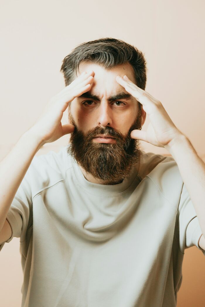 Man with a beard holding his head, appearing stressed or regretful, illustrating driving away potential life partners.