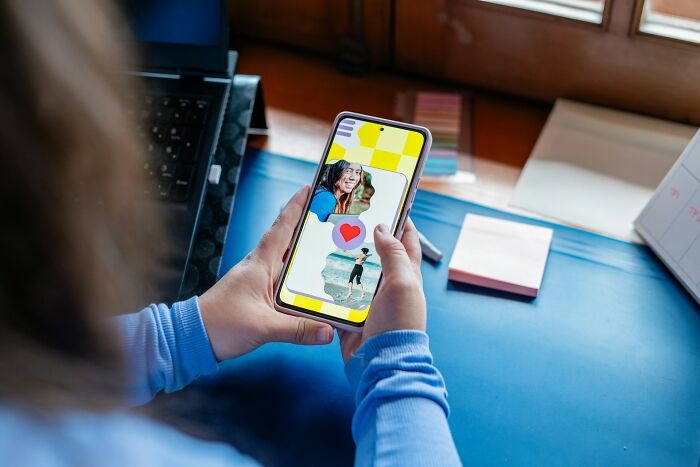 Person using a smartphone with a dating app showing profile pictures and a heart icon, highlighting modern dating challenges.