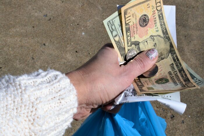 Hand holding cash, coins, and receipts with a blue plastic bag, illustrating useful travel hacks for saving money.