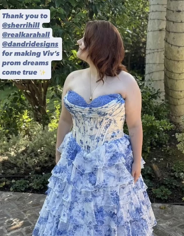 Young woman in a blue floral prom dress, celebrating a major milestone, resembling Melissa McCarthy in an outdoor setting.