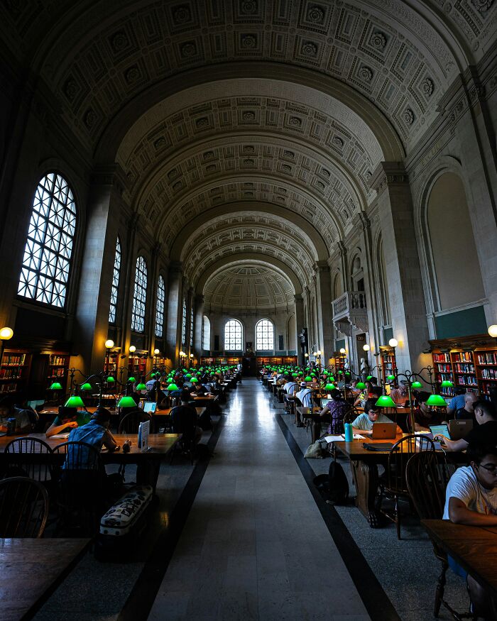 Grand interior of a stunning and impressive library reading room with arched ceilings and green desk lamps.
