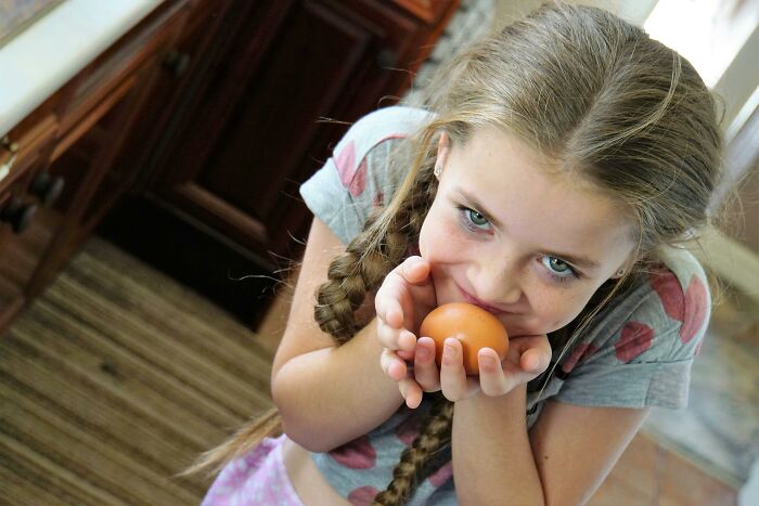 Young girl with braided hair holding an egg indoors, illustrating the concept of baby names that secretly weird people out.