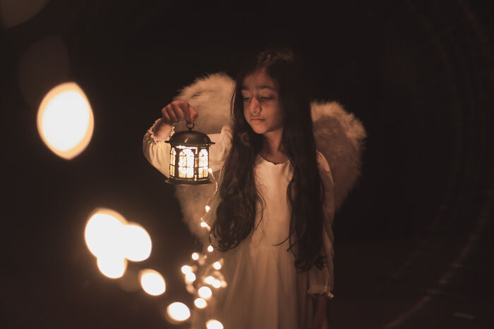 Young girl dressed as an angel holding a lantern with glowing lights, illustrating unique baby names that seem weird.