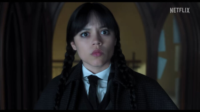 Young woman with braided hair in dark clothing looking surprised in a dimly lit room, representing weird baby names topic.