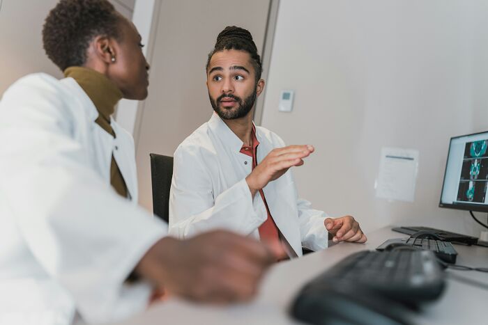 Two doctors in lab coats discussing medical scans on a computer screen, illustrating people ruining their life.