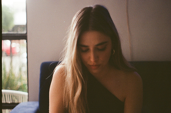 Young woman sitting alone indoors, appearing sad and ignored by family favoring matching triplets.
