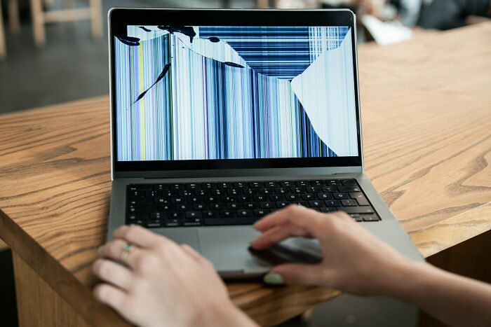 Person with painted nails using a laptop with a c*****d and broken screen showing colored vertical lines.