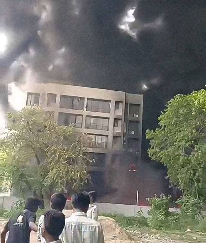 Thick black smoke rises near a building as bystanders watch, related to Air India Boeing jet tech failures incident.