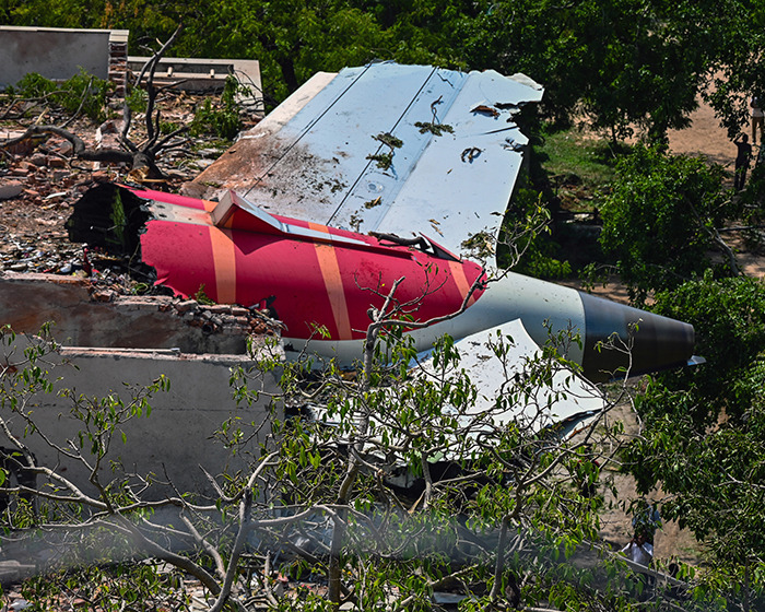 Air India plane wreckage showing damaged tail section surrounded by trees in eerie silence before crash investigation.