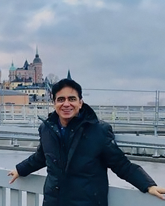 Man in a black coat smiling outdoors with a cityscape in the background, related to Air India pilot hero in tragic crash.