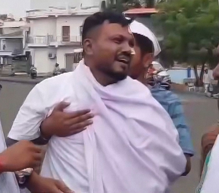 Man wrapped in a white cloth emotionally expressing survivor's guilt as Air India survivor on a street with blurred background.