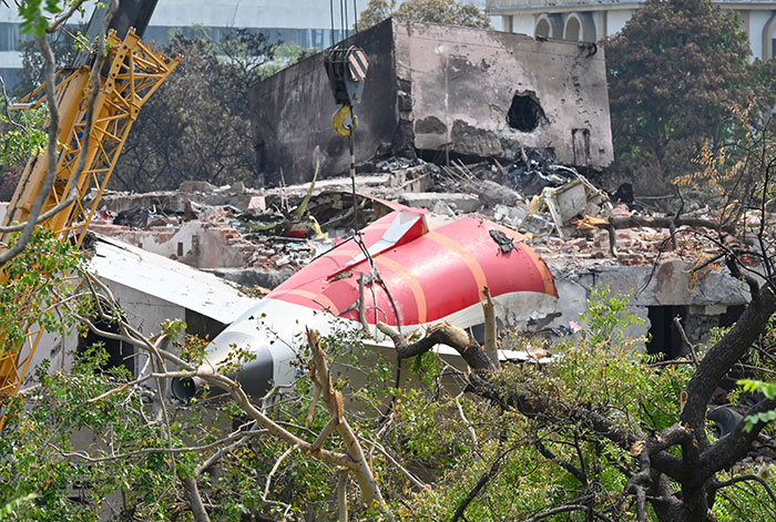 Wreckage of Air India crash amid trees and rubble, showing damaged aircraft parts and rescue equipment on site.